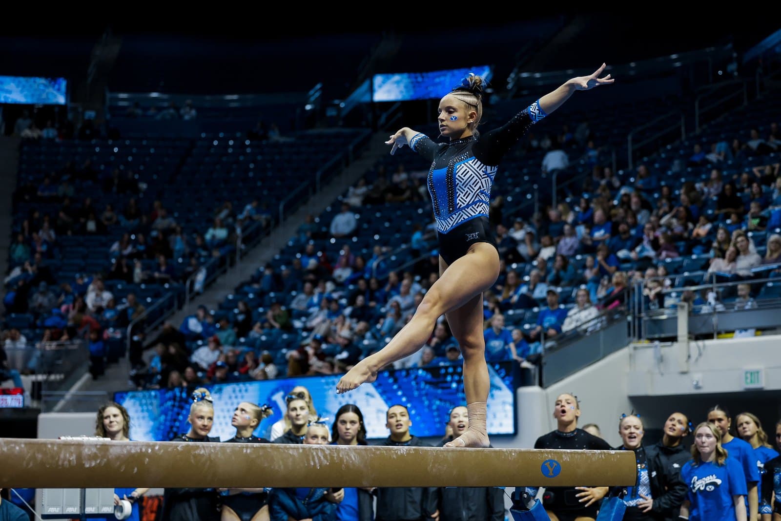 A BYU gymnast extends a leg behind her on the balance beam at the Marriott Center during the Jan. 9, 2026 season opener against Oregon State, with teammates watching from the floor.