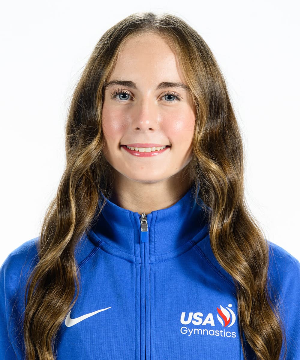 Claire Pease smiles in a blue USA Gymnastics jacket against a white background