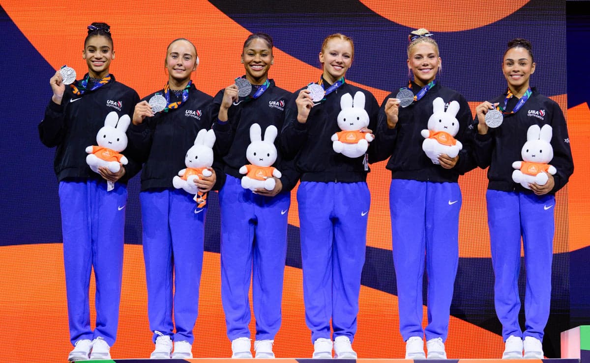 Six U.S. women's gymnasts hold silver medals and Miffy plush toys on the podium at the 2026 World Championships in Rotterdam.