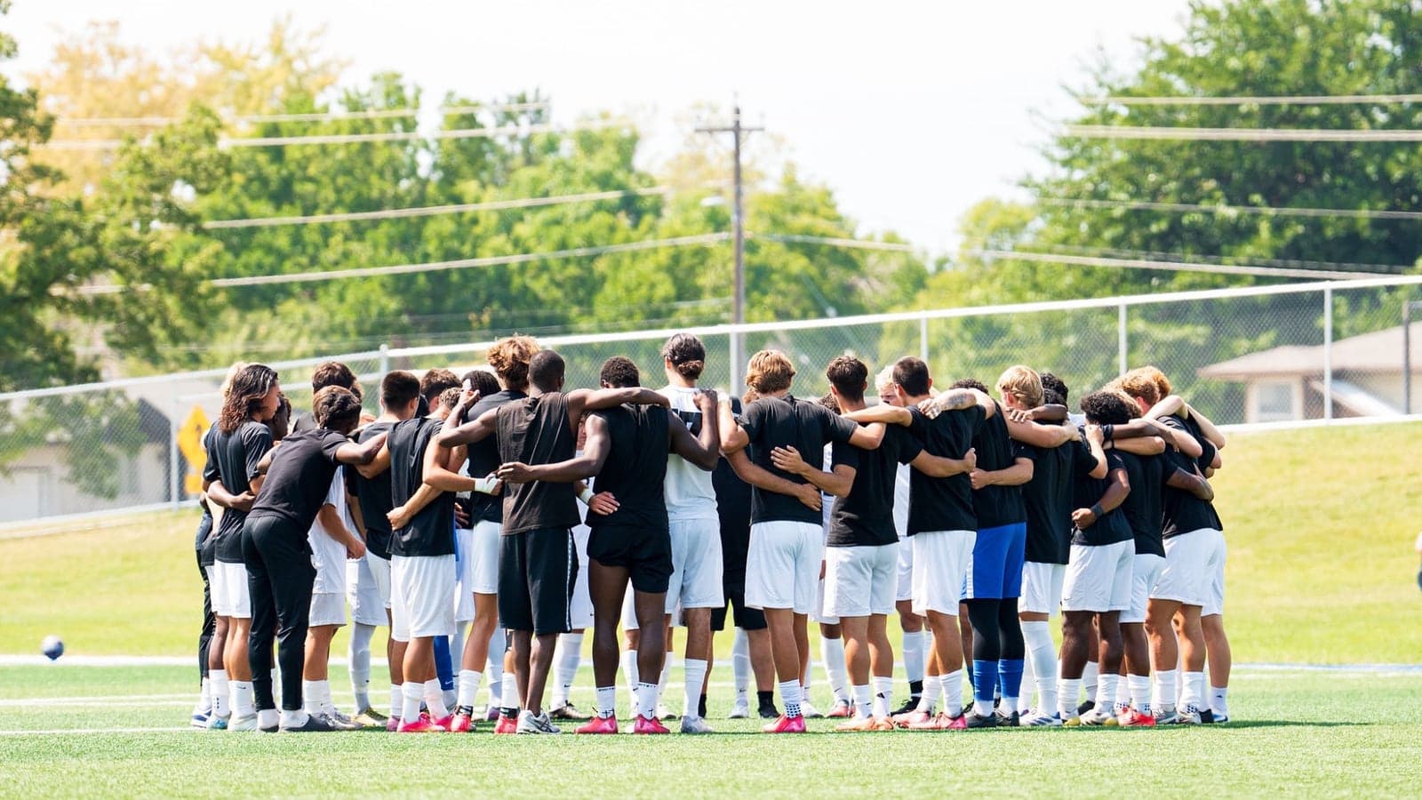 SLCC men's soccer players gather in a team huddle on the field.