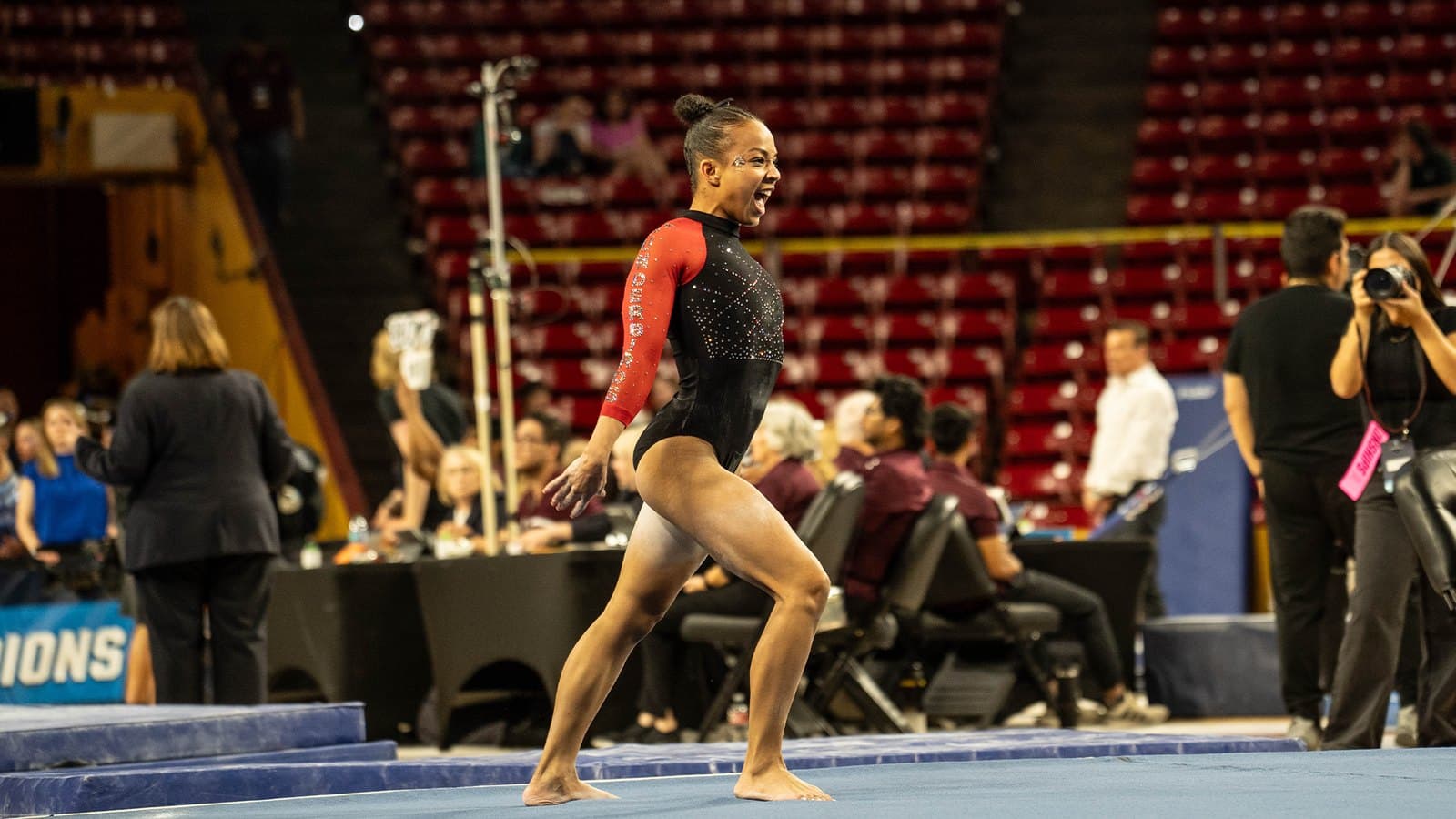 A Southern Utah gymnast in a red-and-black leotard finishes a floor routine as officials watch from the edge of the floor