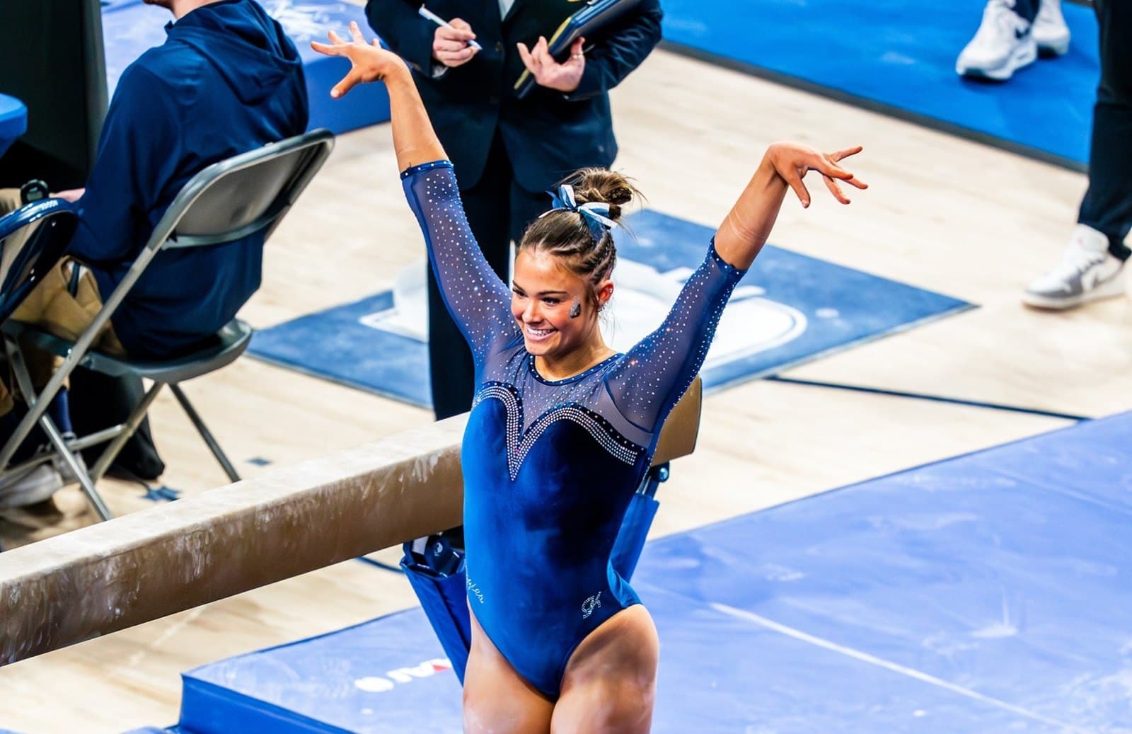 A Utah State gymnast in a navy leotard finishes a routine with both arms raised beside the balance beam during the 2026 season.